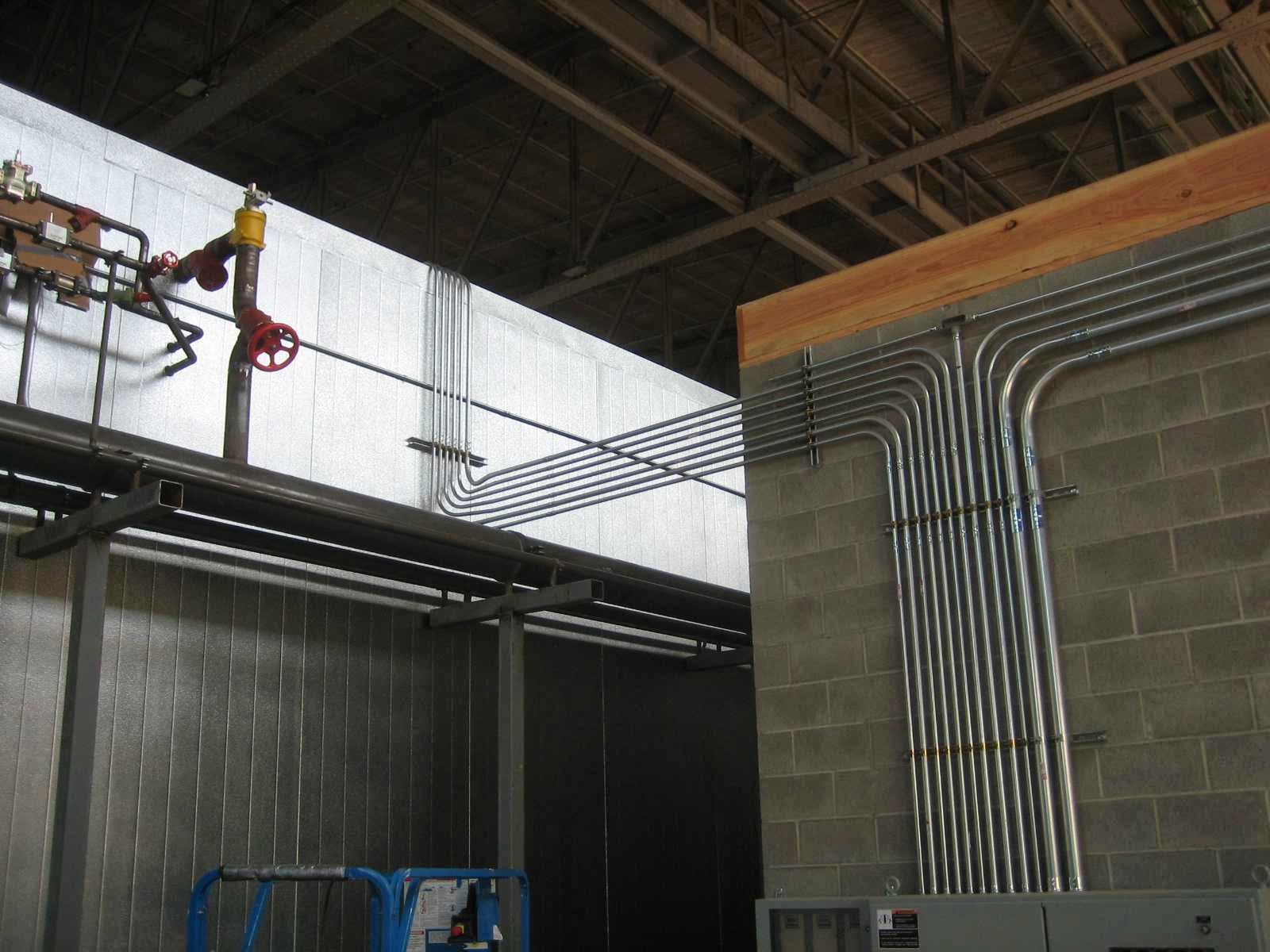 Conduit runs crossing an open commercial ceiling above distribution gear